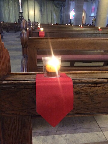 Blick in einen Kirchenraum. In großen Abständen sind Kerzen auf den Kirchenbänken zu sehen.